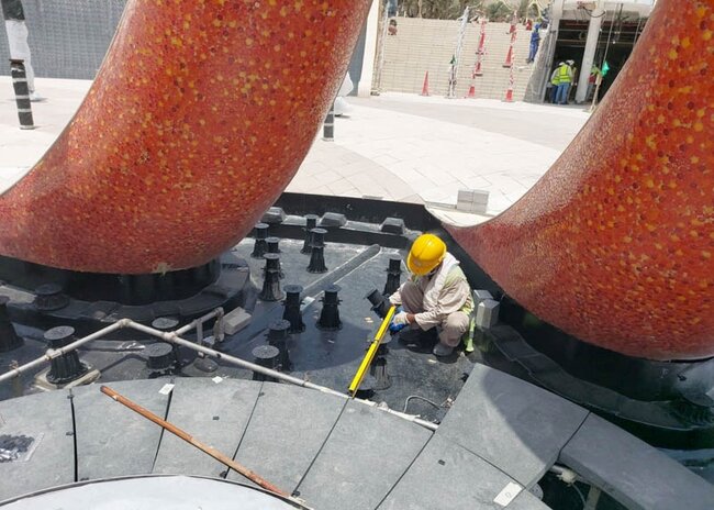 Installer in a yellow helmet calibrating the height of black pedestals