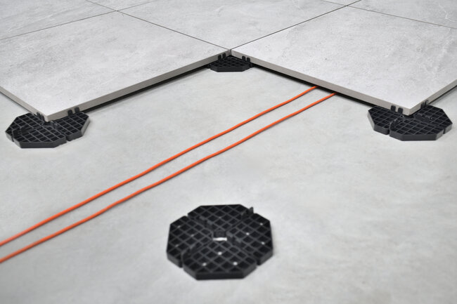 Electrical installation hidden under a raised deck terrace with pavers on fixed-height support pads