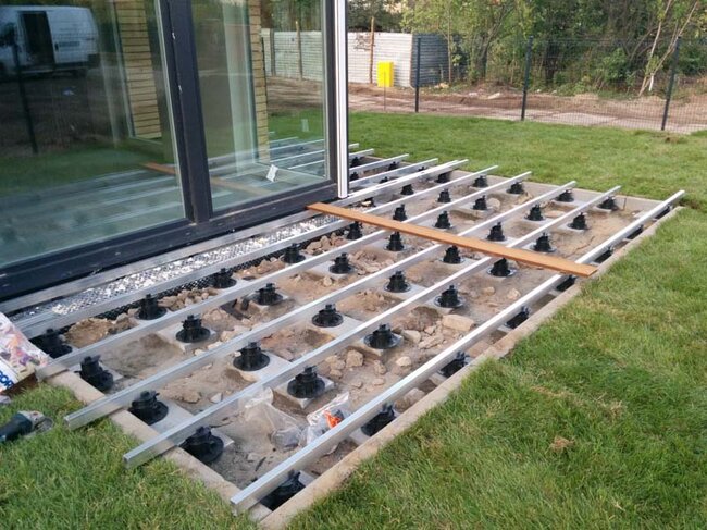 Construction of a raised deck terrace on the ground in the garden with pedestals and composite decking boards