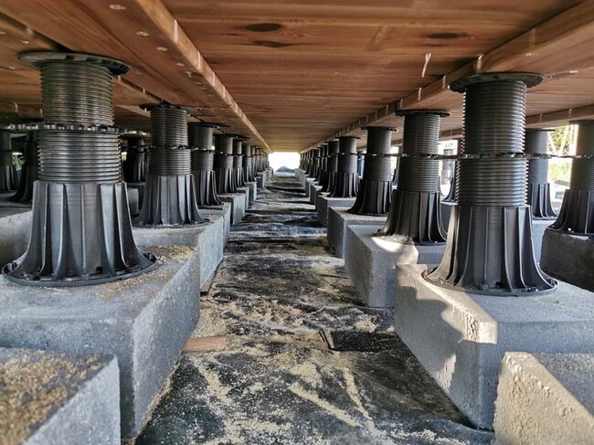 The underside of a raised deck terrace with boards and joists on adjustable pedestals