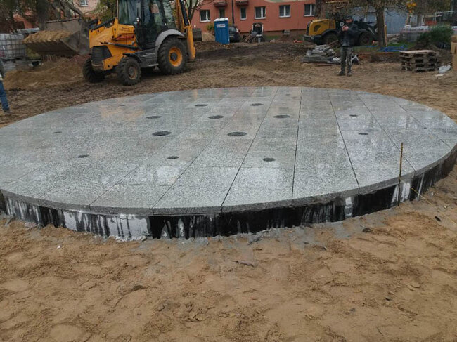 Construction of a round city fountain from gray granite pavers in the square