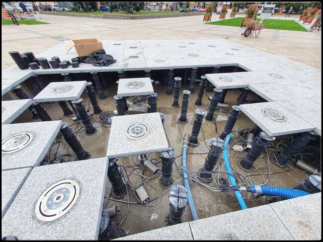 Granite pavers with nozzles laid on tall adjustable pedestals of a raised deck terrace.