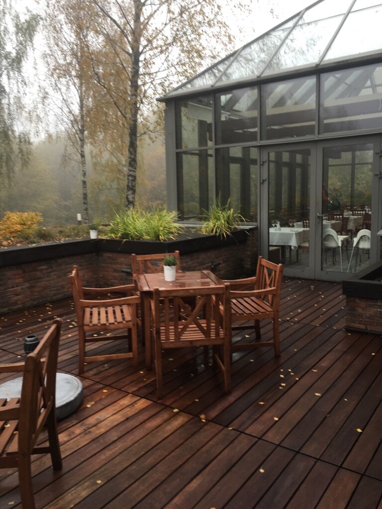 Wooden garden terrace with furniture and a winter garden in the background