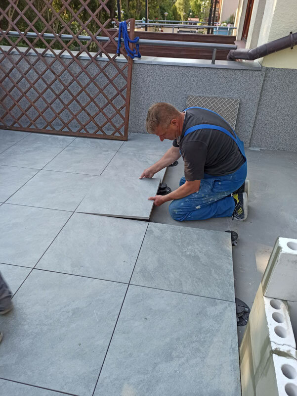 Specialist laying gray porcelain tiles on terrace pedestals