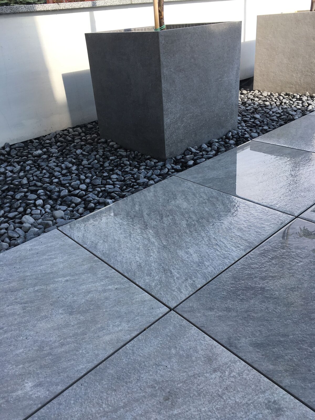 Gray porcelain pavers on a terrace with a stone border and a planter