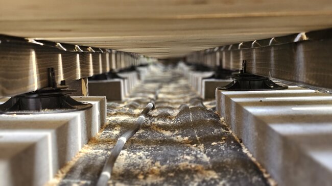 View of the substructure of a wooden terrace on joists and pedestals.