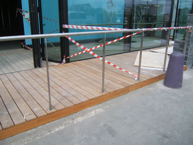 Wooden entrance platform with stainless steel railing at the building.