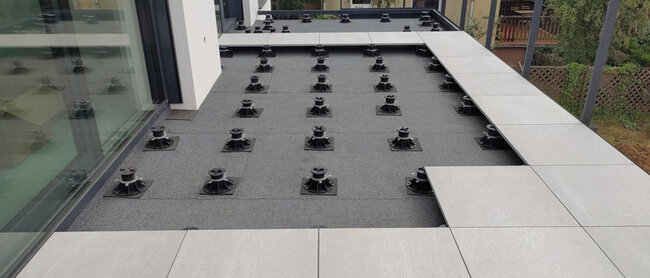 Installation of a raised deck terrace with light gray gres pavers on black adjustable pedestals.