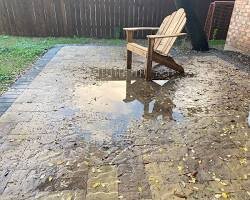 Large puddle on a paved terrace due to poor water drainage.
