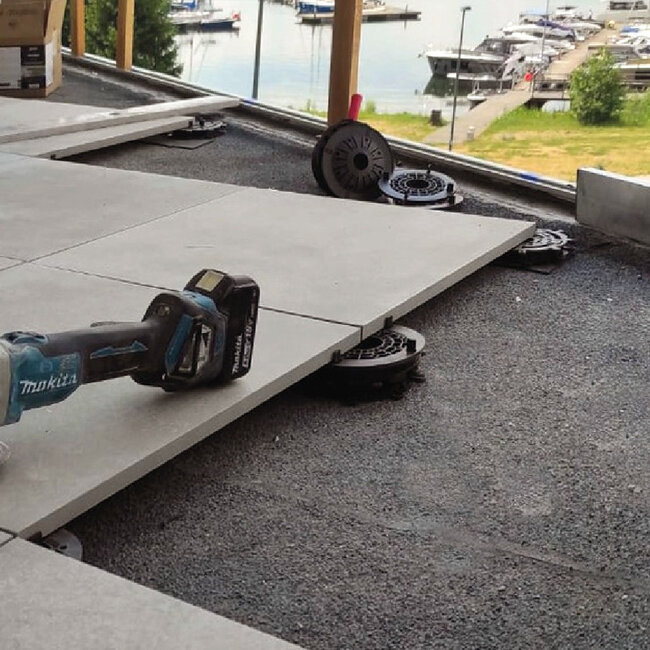 Installing outdoor porcelain deck tiles on low-profile adjustable plastic pedestals with cordless power tool.