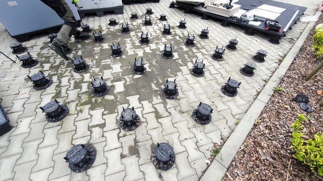 Grid layout of adjustable plastic pedestals placed on paving stones for outdoor terrace installation