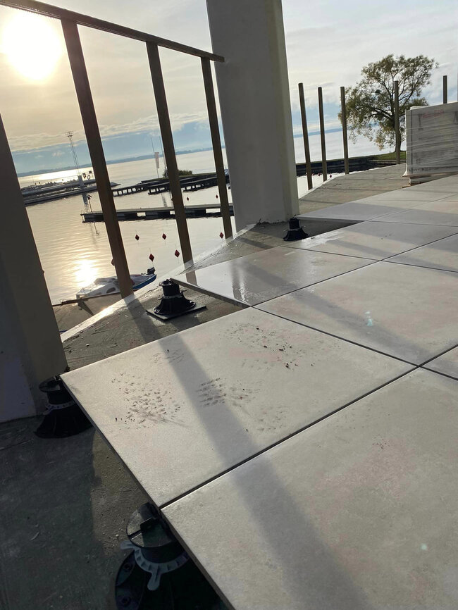 Installation of large grey outdoor patio tiles using an adjustable pedestal riser system overlooking a lake marina.