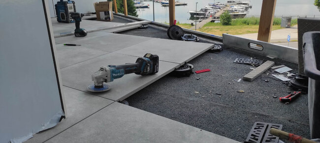 Angle grinder tool placed on raised patio tiles during precise edge trimming on pedestals.