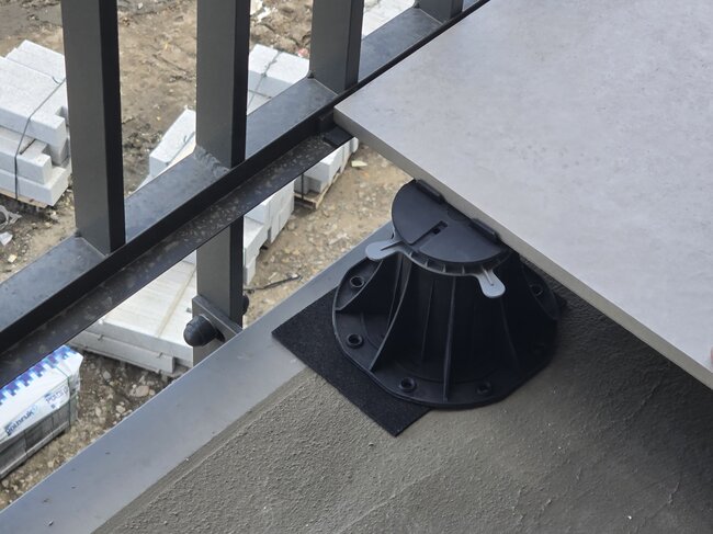 Adjustable plastic pedestal riser supporting a porcelain tile along a balcony edge.