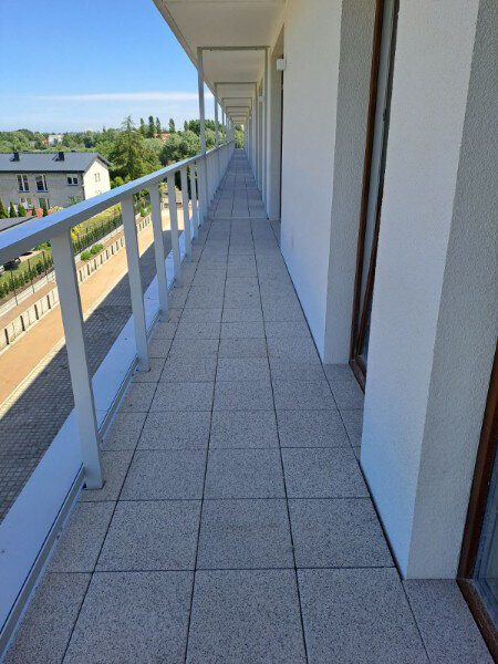 Completed long outdoor terrace flooring with concrete-textured paver tiles and white railings.