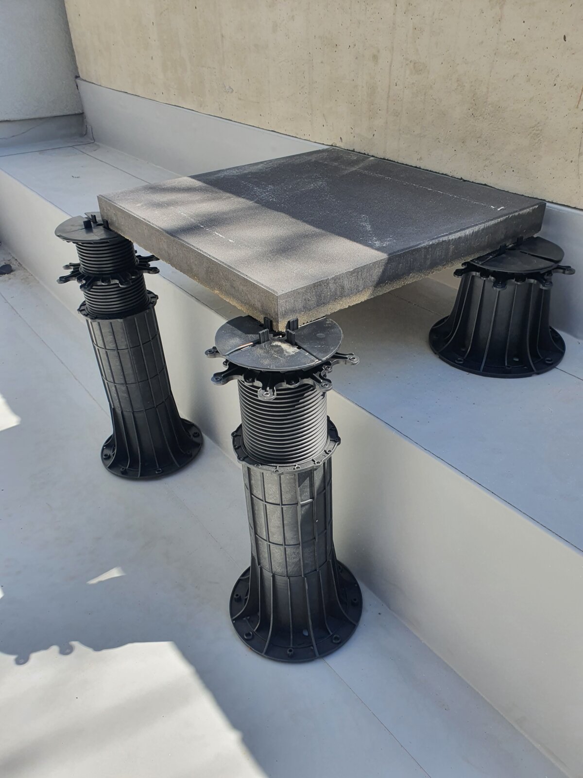 Square concrete paver mounted on adjustable plastic pedestal supports.