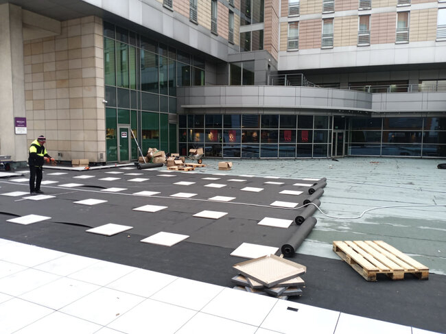 Construction worker installing paver pedestals and base membrane on a commercial building rooftop plaza.