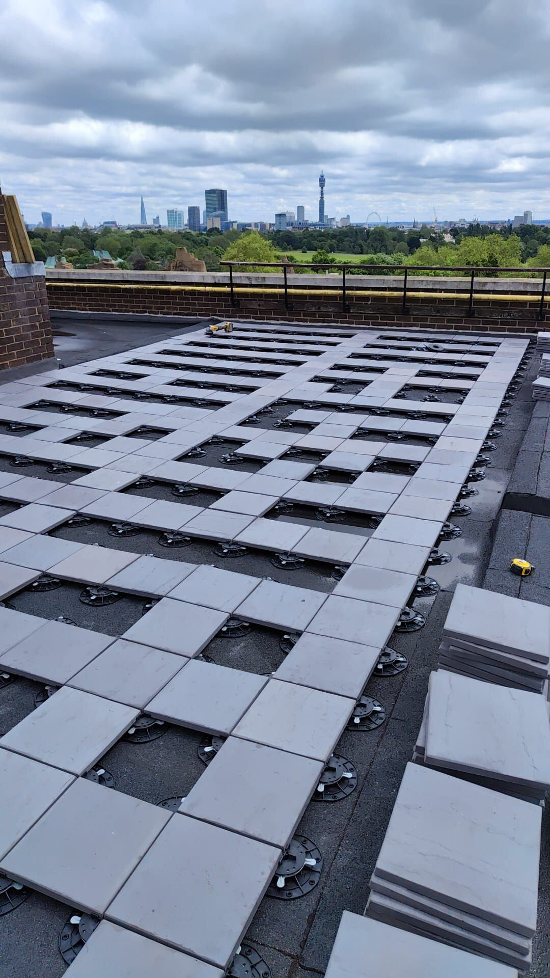 Grid pattern of heavy concrete pavers partially installed on adjustable plastic pedestals for a commercial plaza rooftop terrace.