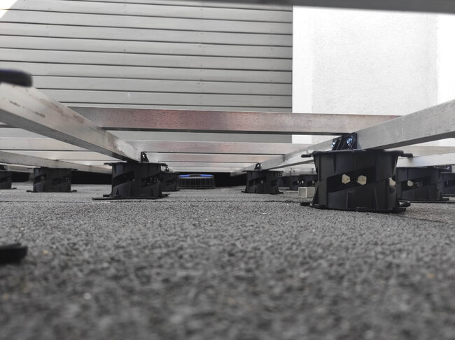 Low-angle view of aluminum deck joists supported by low-profile adjustable pedestals on a roof terrace.
