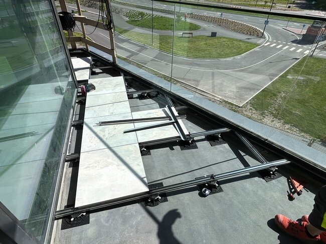 Overhead view of a balcony raised floor installation featuring porcelain pavers on aluminum joists and adjustable plastic pedestals.