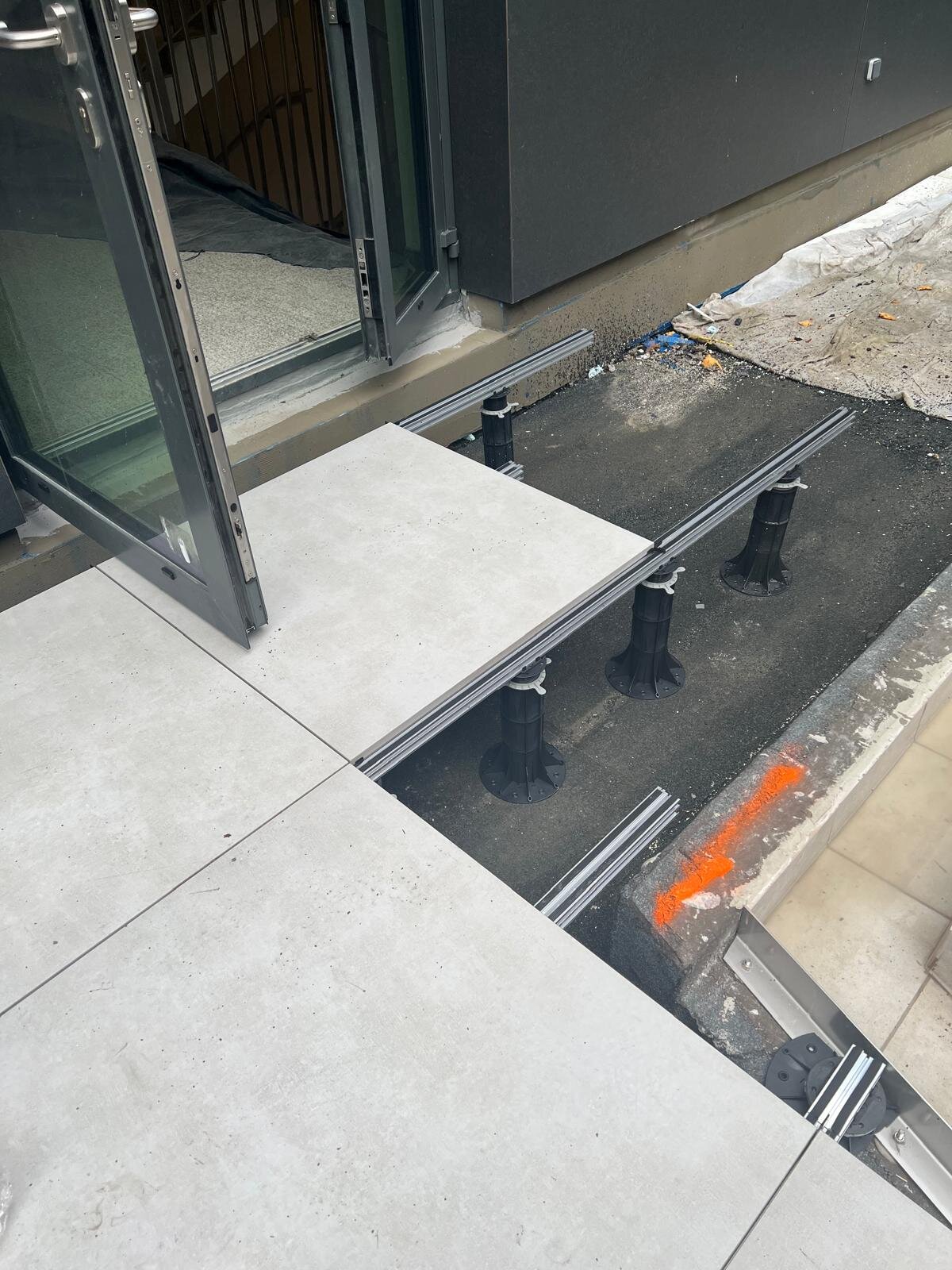 Patio doorway installation showing outdoor porcelain tiles laid on aluminum joists and adjustable plastic pedestals.