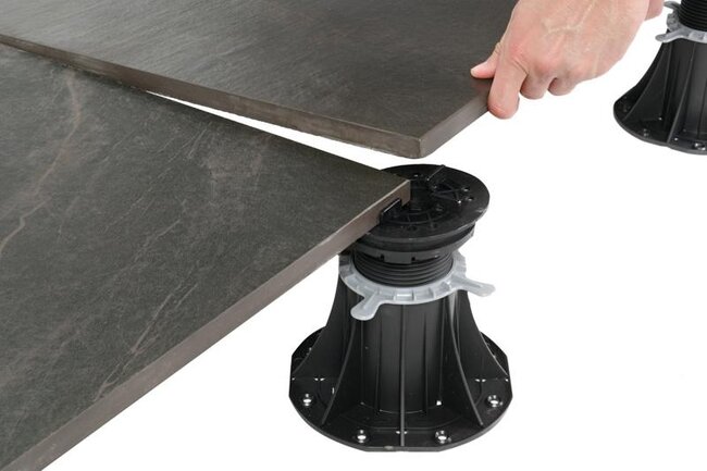Installing dark porcelain paving tiles onto adjustable plastic pedestal.