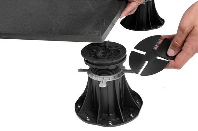 Hand placing a rubber levelling pad or shim onto an adjustable plastic pedestal riser.
