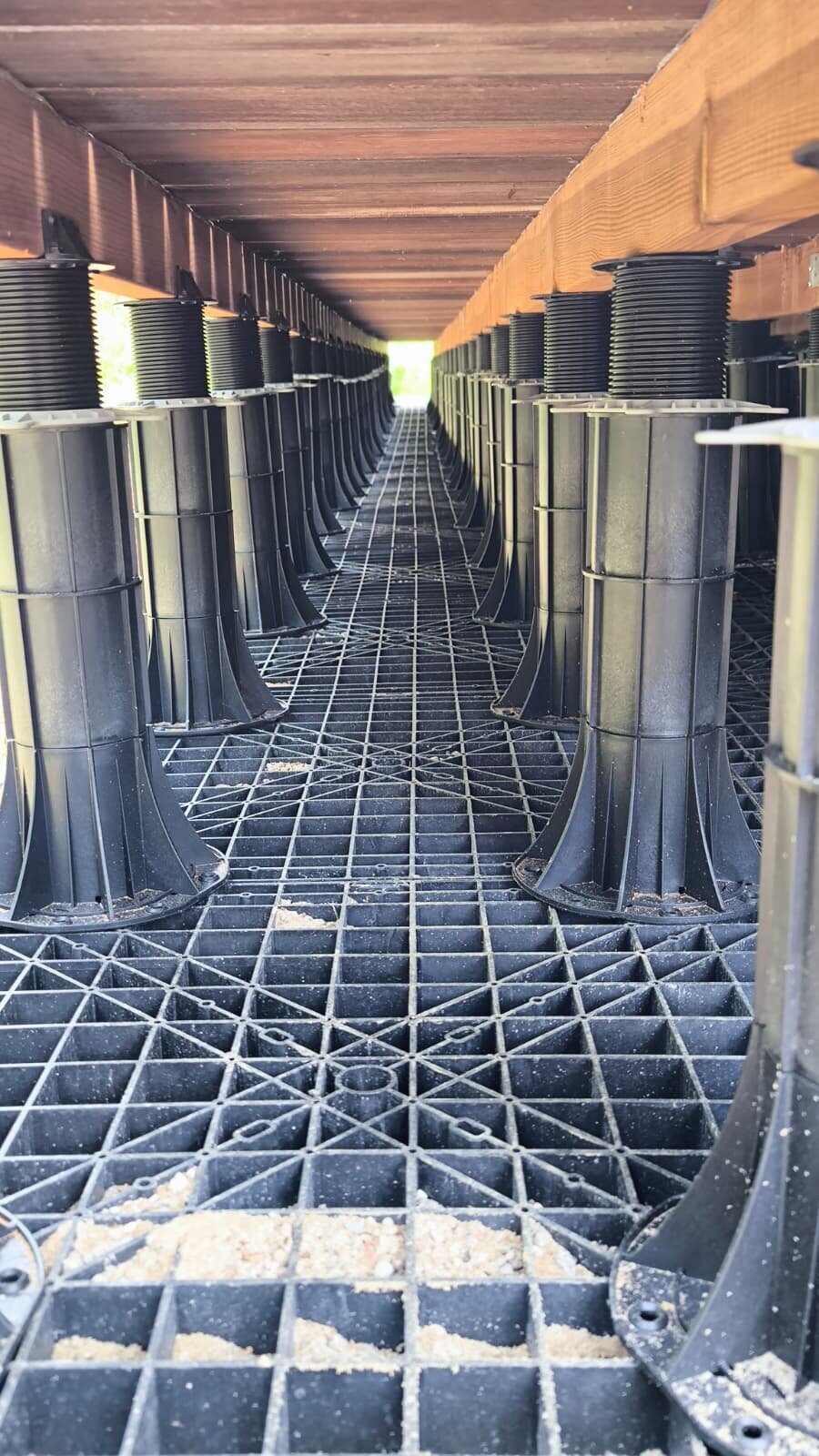 Adjustable plastic pedestal support system installed beneath a roof deck framework.