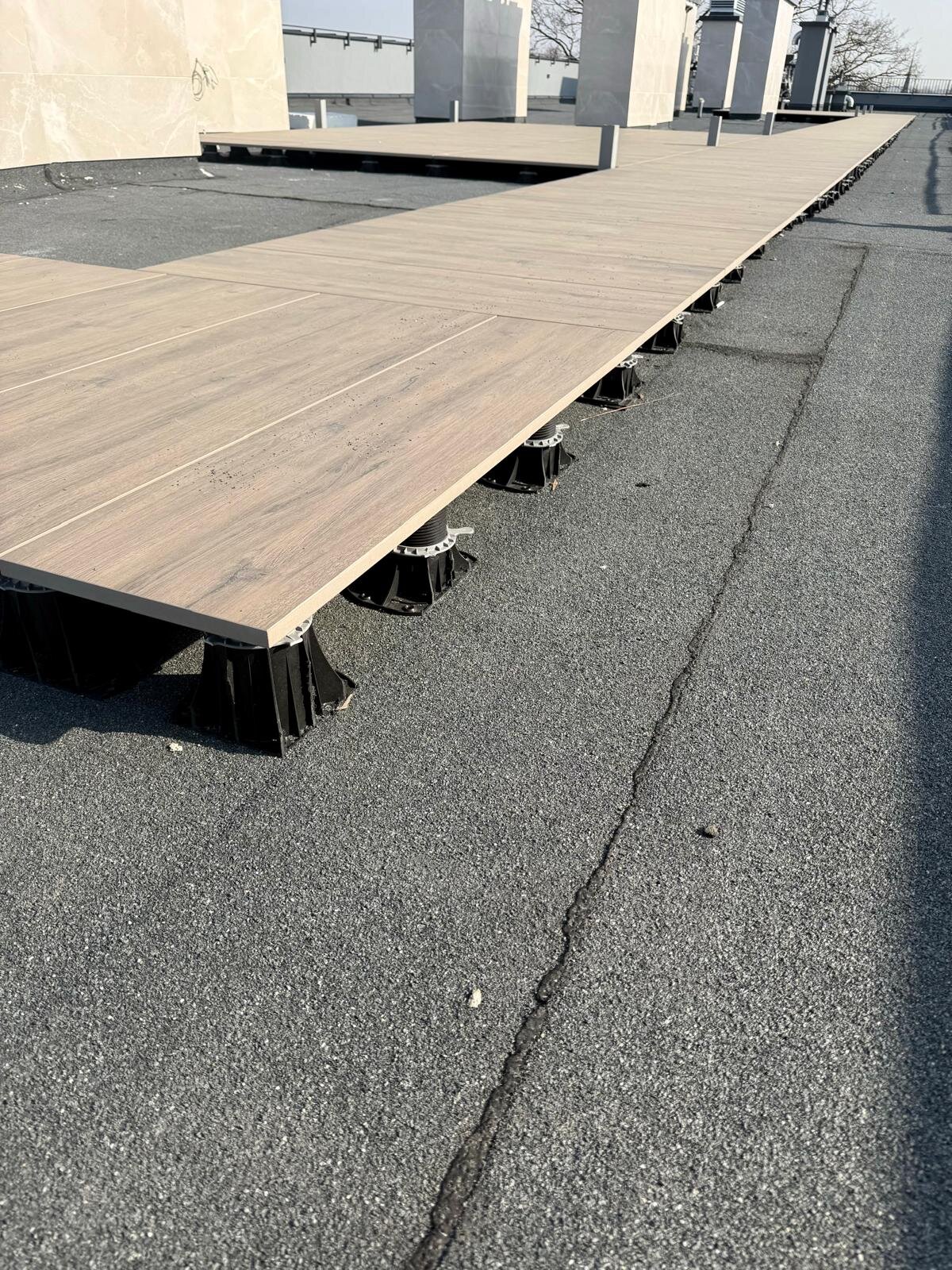 Outdoor porcelain pavers supported by adjustable pedestal risers on a flat roof deck.