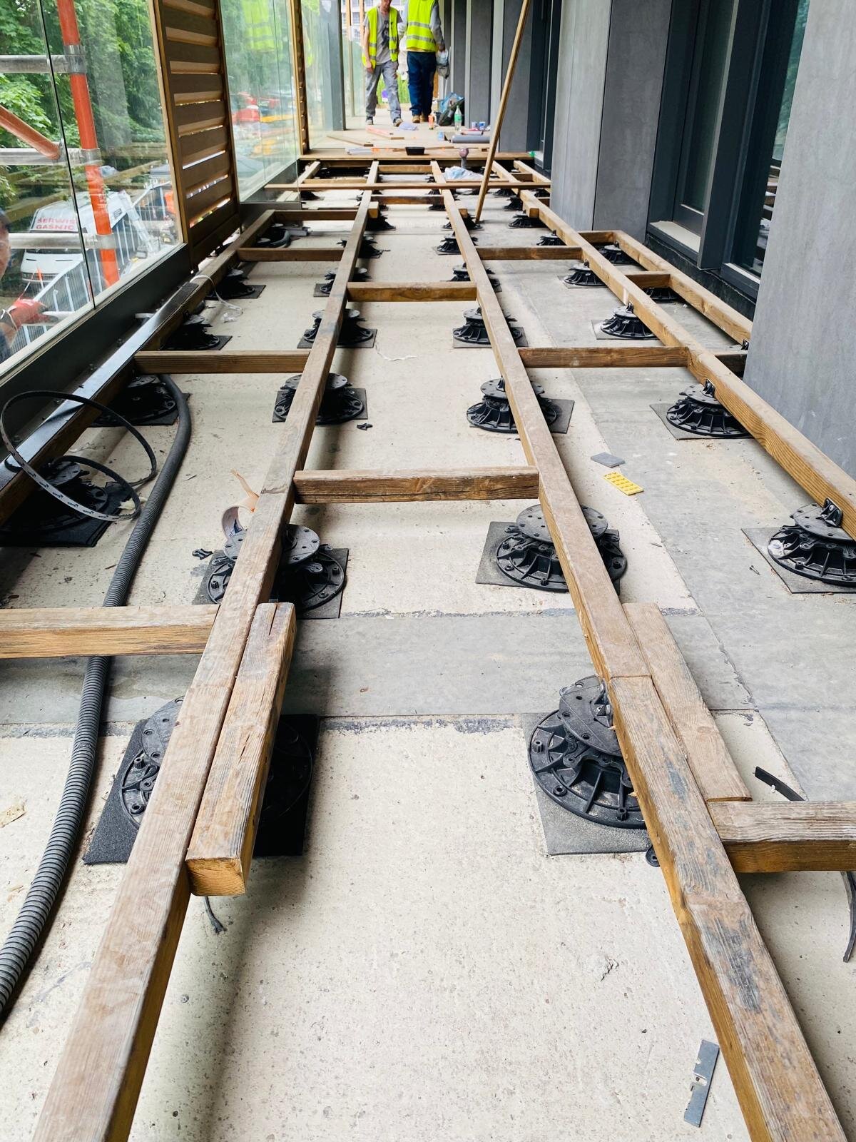 Adjustable pedestal supports and timber joist substructure being installed on a terrace balcony.