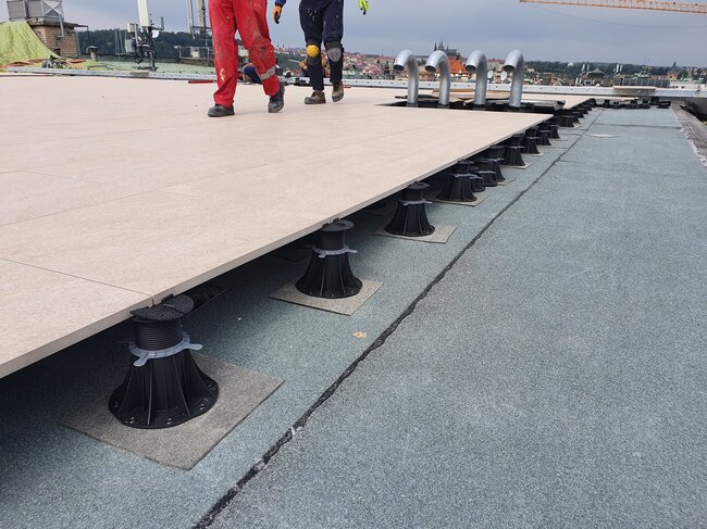 Workers walking on a partially installed raised rooftop terrace paver system supported by adjustable pedestals.