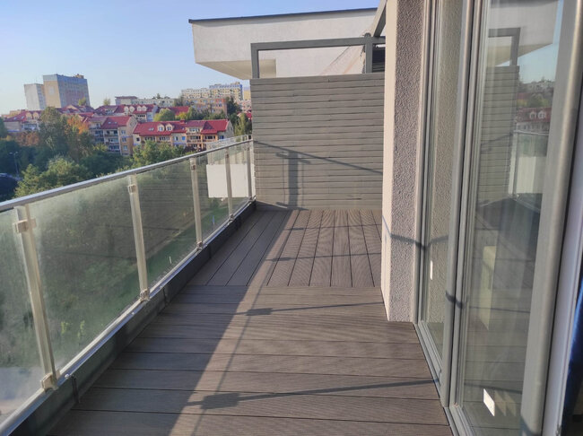 Modern apartment balcony featuring composite wood decking, glass railings, and a privacy divider.