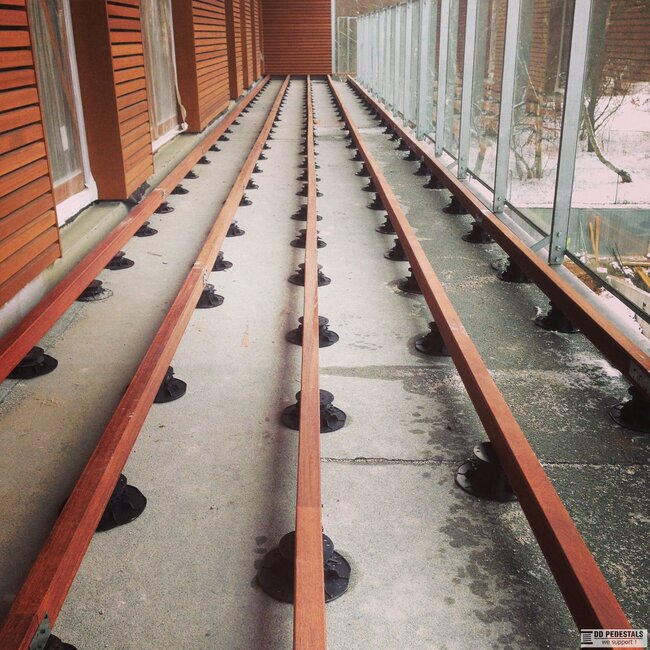 Long balcony deck substructure featuring parallel timber joists mounted on adjustable pedestal supports.