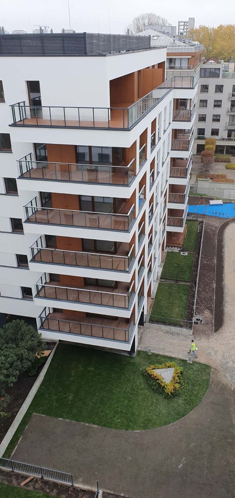 Exterior view of a modern multi-story residential apartment building with wooden-decked balconies and glass railings.