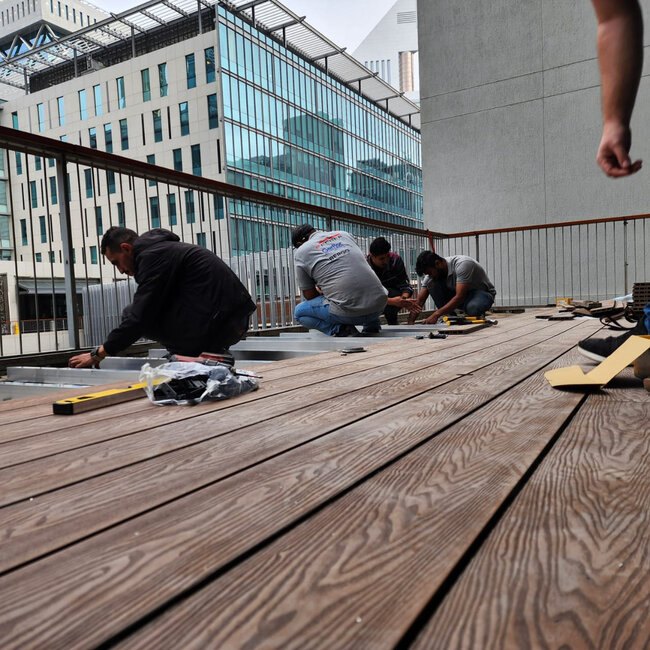 Rooftop terrace deck installation using wood decking on adjustable supports and joists.