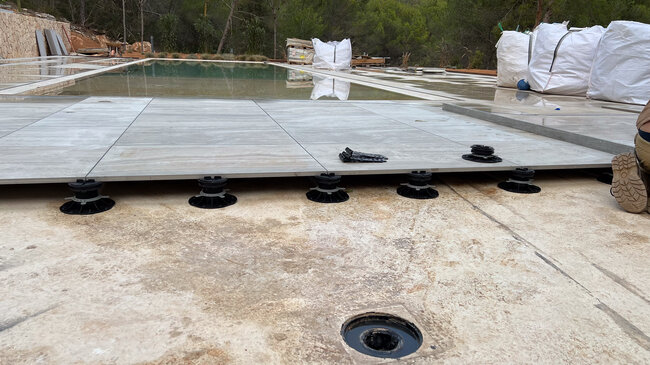 Installation of porcelain pool deck pavers on adjustable pedestal system.