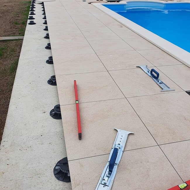 Installing porcelain pavers on adjustable pedestal supports around a pool.