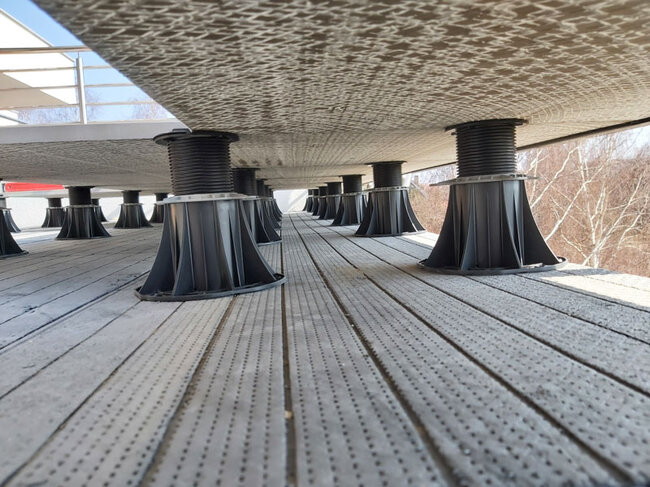 Adjustable deck pedestals supporting a raised patio paver system.