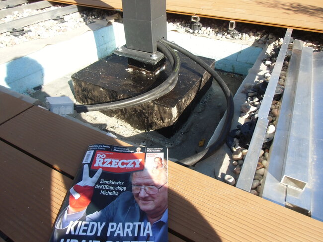 Electrical cable routed along post base and underlying gravel structure beneath elevated terrace decking.