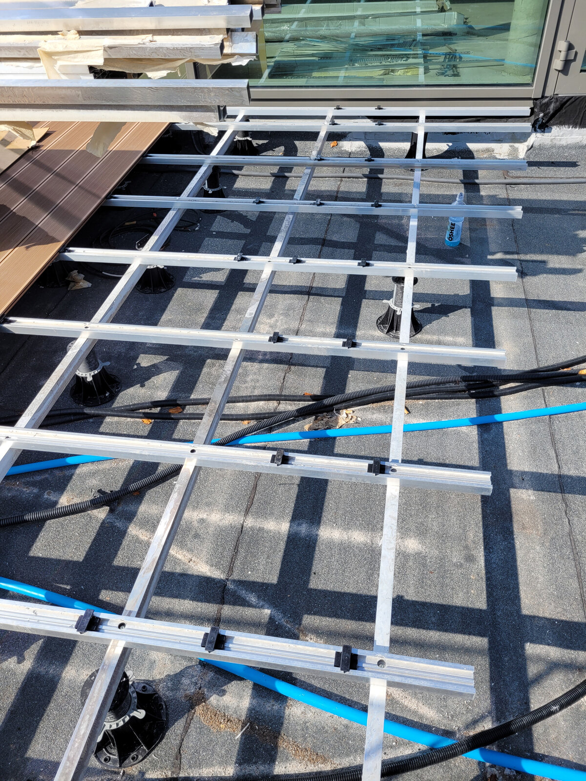 Aluminum joist framework mounted on adjustable pedestals routed over pipes and cabling under a raised deck.