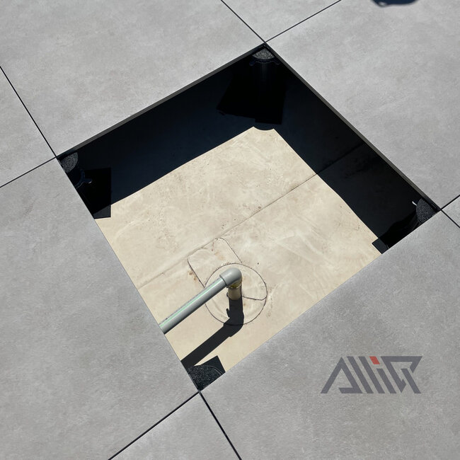 PVC plumbing pipe connected to a roof drain beneath a raised porcelain paver deck.