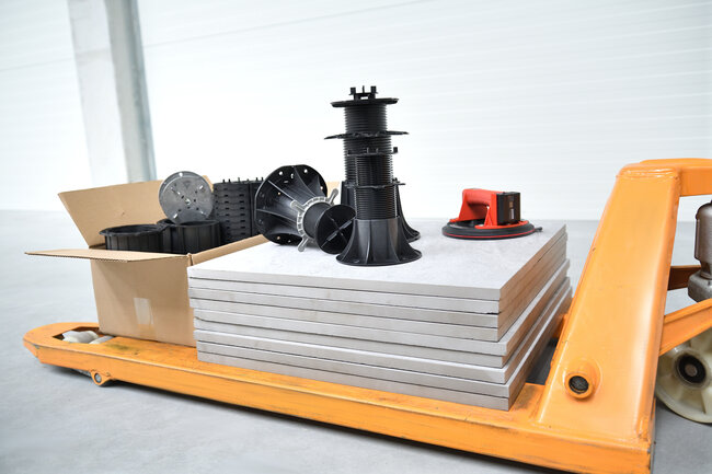 Adjustable deck pedestals stacked with paver tiles for outdoor installation.