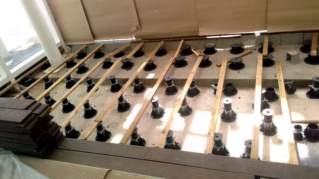 An array of black adjustable pedestals supporting wooden joists during terrace deck construction.
