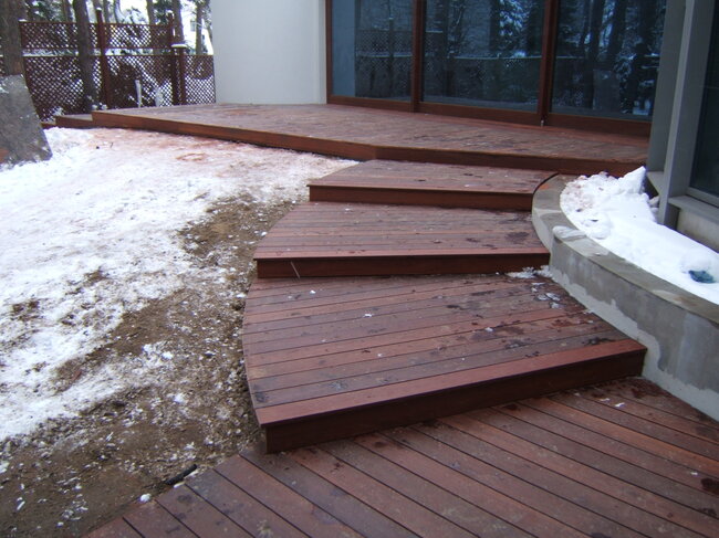 Curved wooden deck steps leading to an outdoor terrace surrounded by snow in winter.