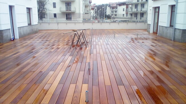 polished wooden terrace deck in an apartment complex courtyard with wet boards and construction sawhorses.