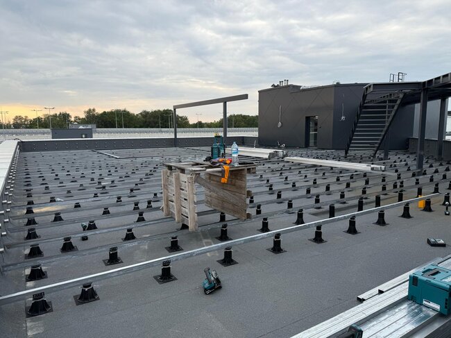 Rooftop deck under construction with adjustable pedestals, metal framing joists, and power tools.