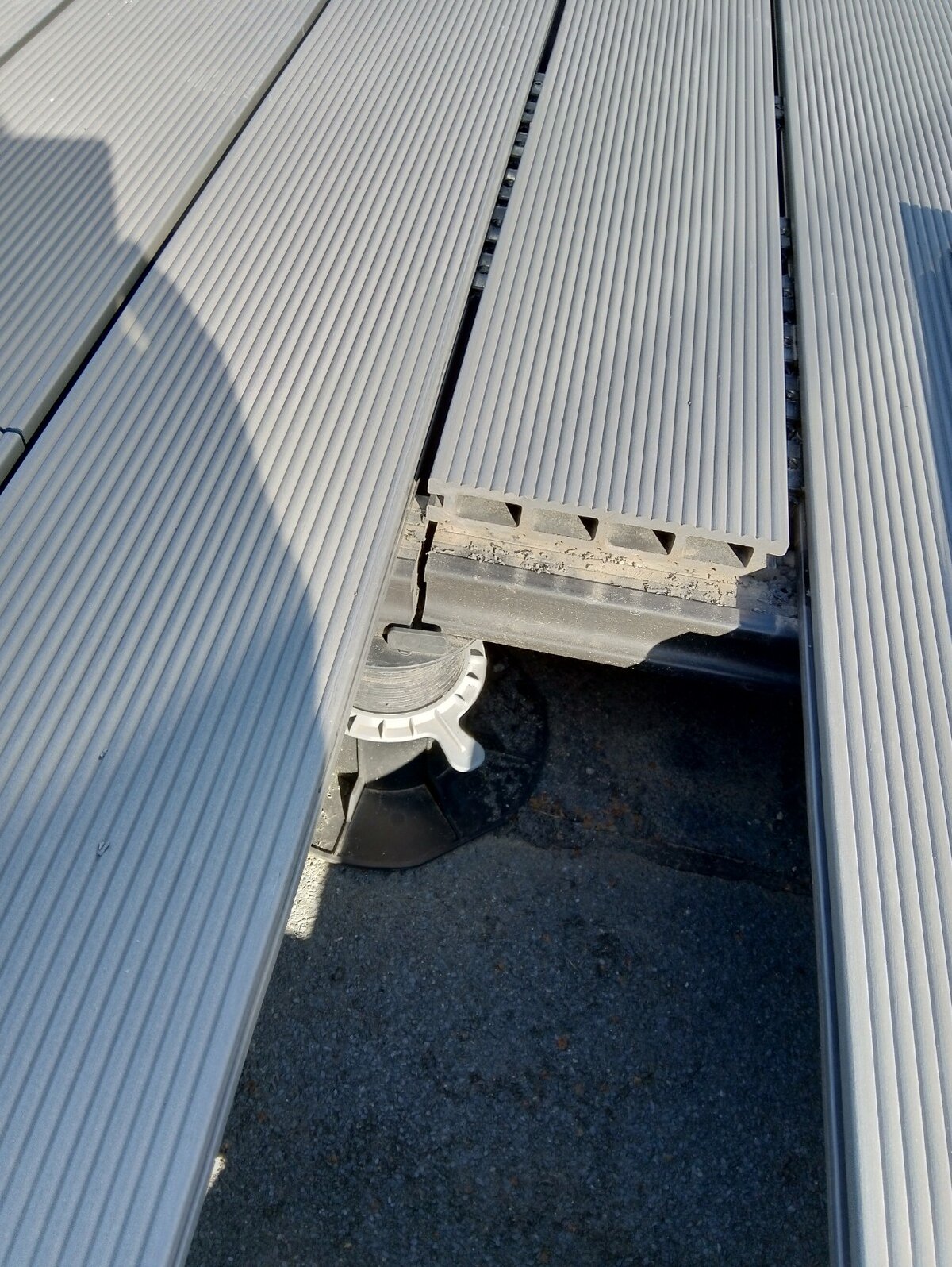 Close-up of grooved grey composite decking boards installed over an adjustable pedestal support.