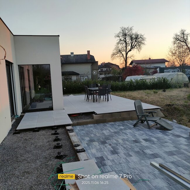 Modern patio installation showing elevated paver tiles mounted on adjustable pedestals next to a cobblestone paved section.