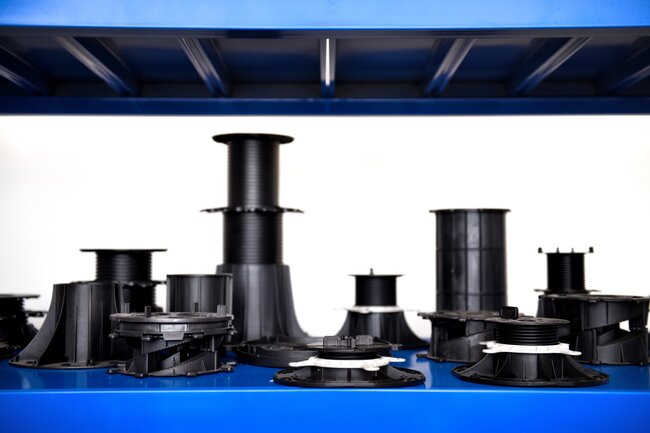 Assorted black adjustable plastic pedestals for deck and paver support arranged on a blue shelf.