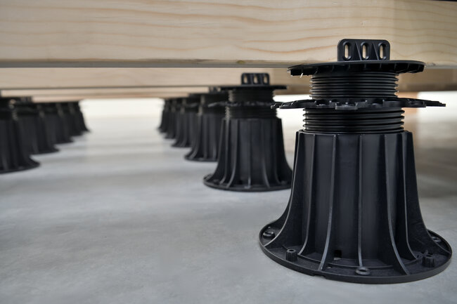 Wooden deck joists supported by adjustable black plastic pedestal risers.